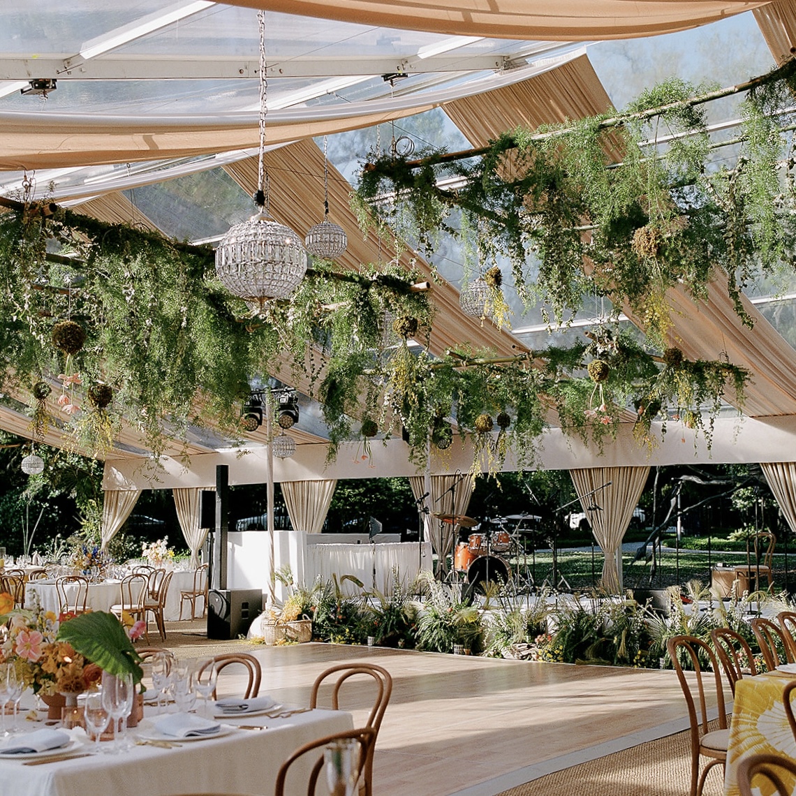 Elegant wedding tent surrounded by lush greenery with glowing chandeliers at the NOMA Sculpture Garden in New Orleans.