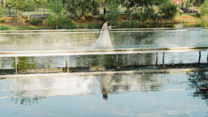 Bride and her father walking across a bridge at the NOMA Sculpture Garden with their reflection in the water.
