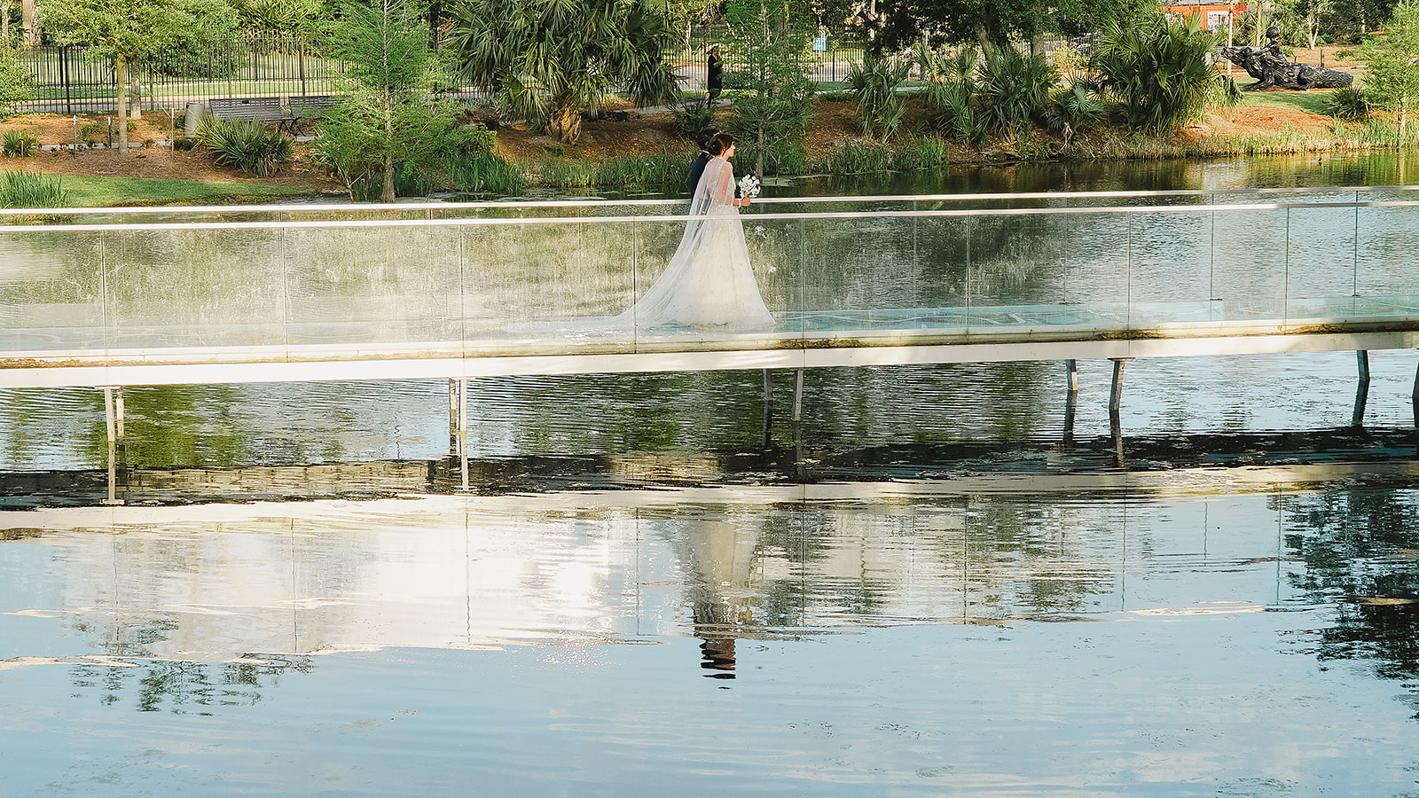 Bride and her father walking across a bridge at the NOMA Sculpture Garden with their reflection in the water.